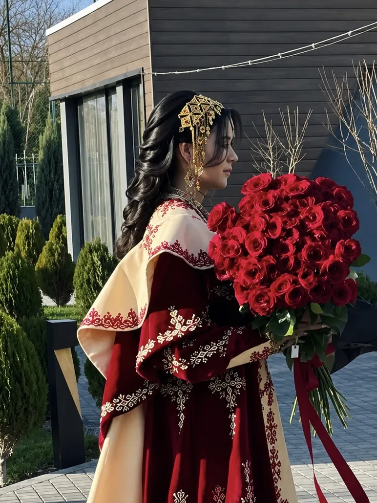 Selbi gyrmyzy lybasda, keşdeli ak ýapynjada, elinde gyzyl bägüller